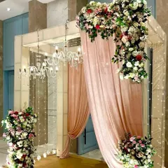 An elegant and grand entrance designed for a wedding or reception. The decor features soft pink draping, cascading floral arrangements with roses and greenery, and sparkling chandeliers that create a luxurious and welcoming ambiance for your guests.