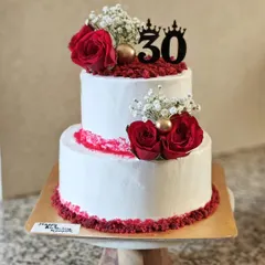 A classic and elegant choice for a 30th birthday or an intimate wedding. This two-tier red velvet cake is frosted with white ganache and whipped cream, and simply decorated with fresh red roses and red velvet crumbs.