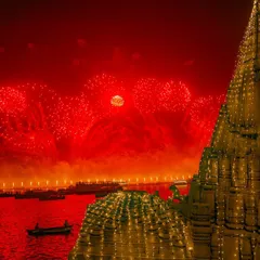 Fireworks explode in a red-tinted sky over a beautifully illuminated temple during Dev Deepawali in Varanasi. This festival of lights transforms the city into a divine spectacle.