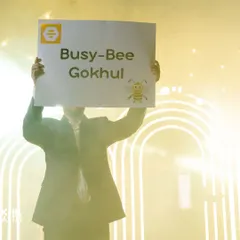 A friend holds up a "Busy-Bee Gokhul" sign, a fun and personal prop used to tell the couple's story.