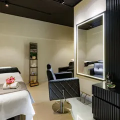 The hair-cutting station is designed for style and comfort. It features a luxurious tufted leather chair and a large, brightly lit mirror, set against a backdrop of black fluted panels and a dark ceiling for a dramatic, high-end look.