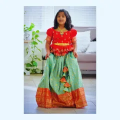 Our client from the USA looks gorgeous in her turquoise Kanchi pattu lehenga. The red maggam work blouse adds a pop of color, and the traditional gold border gives it a festive finish.