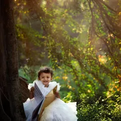A fairytale moment captured outdoors. This toddler looks like she's reading a storybook in an enchanted forest. The sunlight filtering through the trees creates a beautiful, dreamy effect for this toddler portrait.