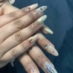 For when you want to make a statement. These long, almond-shaped nail extensions feature a mix of nude polish, dazzling gold glitter, and carefully placed rhinestones for a truly luxurious and festive feel.