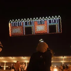 An audience watches our drone formation of a traditional Kuwaiti building. We specialize in creating detailed architectural renderings that celebrate local heritage during our international shows.