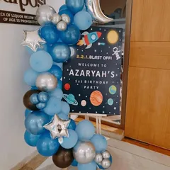 A welcome sign for a space-themed first birthday party. The sign reads "3..2..1..Blast Off!" and is decorated with a matching blue and silver balloon garland.