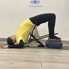 This is Chatushpadasana (Four-Footed Pose) using a chair and blocks for support. This modification helps build strength in the back and legs while ensuring the neck and shoulders remain relaxed. It is an excellent preparation for deeper backbends.