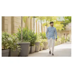 A wide shot of the groom walking in a beautifully landscaped area. This candid-style portrait captures his relaxed and confident demeanor.