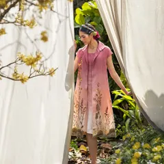 A campaign shot for "When Angels Dream," this look features a layered, hand-painted dress in a lush garden setting. The styling creates a soft, ethereal mood, blending the garment seamlessly with its natural surroundings.