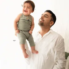 A father lifts his laughing baby boy high in the air. The clean white background emphasizes the joy and connection in this classic father-son portrait.