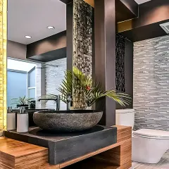 A bathroom design that uses natural and rustic elements for a unique look. The stone vessel sink sits on a wooden vanity, complemented by textured tile walls and warm lighting.