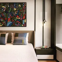The second apartment features a more modern and art-focused design, with a bold painting serving as the centerpiece of the bedroom.