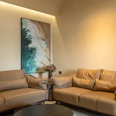 The main seating area with plush, tan leather sofas. A large abstract painting adds a splash of color, while cove lighting provides a warm, ambient glow to the room.