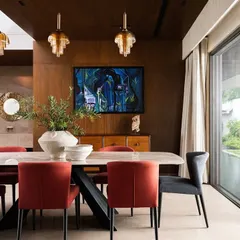The dining space in Villa Shakthi is defined by rich wood tones and bold red chairs, creating an inviting atmosphere for meals. A large sliding glass door opens to the garden, reinforcing the home's connection to its tropical surroundings.