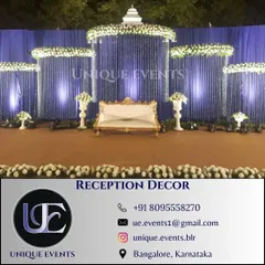 This outdoor reception stage showcases a modern and elegant design. We used a deep blue backdrop with cascading white floral and crystal strings, complemented by classic white urns and uplighting to create a sophisticated look.