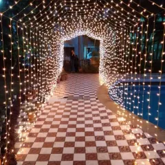 A magical fairy light tunnel created for an evening party entrance. This arched walkway, leading to a poolside area, is made entirely of warm string lights.