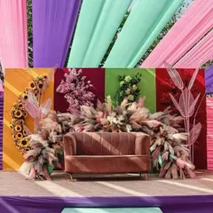 A colorful stage backdrop for an engagement, featuring panels of different colors, pampas grass, and bright floral arrangements.