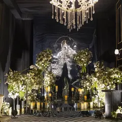 A royal entrance with a classy arrangement of florals. A reflective, textured backdrop is flanked by masses of white flowers and candles, creating a glamorous and dramatic effect.