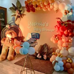 This cozy and rustic baby shower theme features a large teddy bear, a wicker peacock chair, and a personalized backdrop. The organic balloon arch in pastel and earthy tones completes the warm and inviting look.