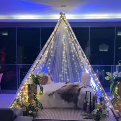We transformed a simple balcony into a romantic boho-themed escape for an anniversary. This cozy teepee, draped in fairy lights and surrounded by rustic floral arrangements, creates a perfect intimate setting against the city lights.