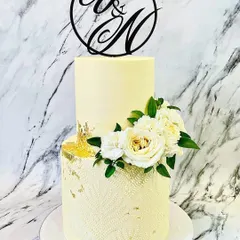 For a classic and romantic wedding, I created this elegant two-tier buttercream cake. The design features a subtle textured pattern on the bottom tier, touches of gold leaf, and a beautiful arrangement of fresh white roses and carnations, all topped with a custom "Y&N" monogram.