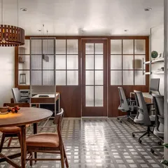 This view of the 'On The Grid' office showcases the open and organized environment we created. The workspace features shared desks with clean lines, separated from the meeting area by a perforated metal screen. A custom wooden pendant light adds a touch of warmth to the minimalist design.