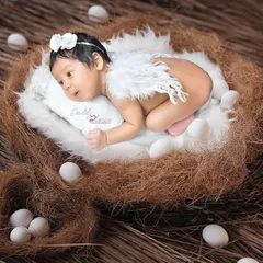 A creative newborn photo with the baby posed with small angel wings, resting in a cozy nest prop surrounded by decorative eggs. This is a beautiful way to capture their angelic look.