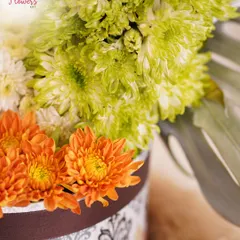 A detailed close-up of the heart-shaped arrangement, focusing on the texture of the green chrysanthemums and the vibrant orange daisies below. This shows the precision required for such a creative floral design.