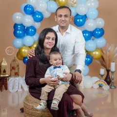 A happy family of three. This studio portrait captures the joy of a young family celebrating their baby's first milestone, surrounded by a festive balloon setup.