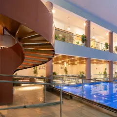 A view across the pool towards the spiral staircase at the Sona Vistaas Clubhouse. The design creates layers of activity, with the calm blue of the water contrasting with the warm tones of the staircase and upper-level gathering spaces.