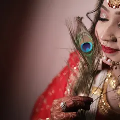 A creative and artistic bridal portrait using a peacock feather as a prop. This close-up shot highlights the bride's flawless makeup and serene expression.