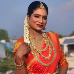 A stunning portrait of a dusky bride against a blue sky. The makeup is kept natural and glowing, with a bold red lip that complements her beautiful skin tone and orange saree.