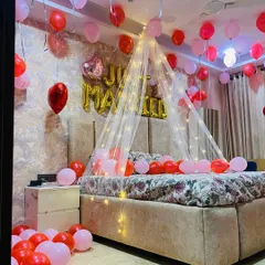 A 'Just Married' room decoration to welcome the newlyweds. The setup includes a bed canopy with fairy lights, red and pink balloons, and a rose petal heart on the floor.