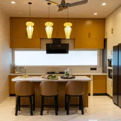 A full view of the 'Sukoon' kitchen, featuring mustard-yellow cabinets, a white quartz island, and unique pendant lights.