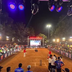 The view from behind the batsman during a night match. You can see the crowd, the powerful overhead lights on the truss, and the main stage with the LED screen, creating a professional tournament atmosphere.