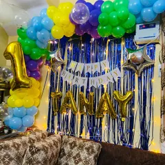A vibrant first birthday decoration I did at home for a baby named Tanay. The backdrop includes a colorful balloon arch and a blue tinsel curtain with fairy lights.