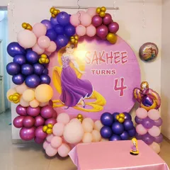 A Rapunzel-themed fourth birthday party featuring a custom circular backdrop with the princess herself. The scene is framed by an organic balloon garland in shades of purple, pink, and gold, matching Rapunzel's dress and hair.
