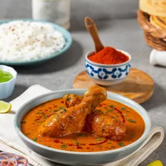 A vibrant chicken curry for Rakesh Masala. The styling includes key ingredients like red chili powder and fresh herbs to tell a story about the dish's flavor.