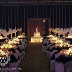 A glamorous anniversary celebration with a dramatic red and black theme. The room is filled with candlelit tables, large white feather centerpieces, and a stunning stage with a heart-shaped light installation.