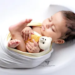 A baby boy cuddles his tiny teddy bear, swaddled in white and yellow. A simple, heartwarming portrait.