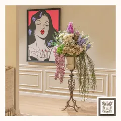 This lush artificial floral arrangement brings nature indoors in the most enchanting way. Placed on a tall metal pedestal, it adds a dramatic and elegant touch to this corner, complemented by playful pop art.
