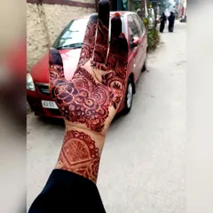 A candid shot of a beautiful henna stain. This shows the back of the hand, where the design features a lovely mandala and detailed finger work, all in a rich mahogany color.