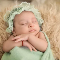 A sleeping newborn wears a delicate mint-green lace bonnet, her hands gently crossed. This image highlights our attention to detail, using soft props and accessories to add a touch of elegance to the portrait.