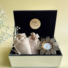 Elegance in a box. This luxe glass hamper contains fragrant potli bags and a beautiful flower-shaped brass diya, perfect as a sophisticated and minimalist Diwali gift.