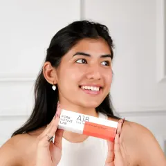 A bright, happy lifestyle portrait of a model holding the skincare product. Her genuine smile and radiant skin connect the brand with feelings of confidence and self-care.