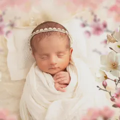 A simple and beautiful close-up. The focus is entirely on the baby's face, framed by a soft white wrap and a delicate headband, highlighting their peaceful sleep.