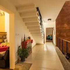 An exposed brick accent wall brings texture and warmth to this hallway in the Reshma Residence. It contrasts with the clean white walls and serves as a backdrop for the home's central staircase, guiding movement through the space.