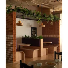 In a busy office, creating zones for quiet work or leisure is key. This seating niche uses raw hollow bricks and an overhead mesh for plants, blending an industrial vibe with biophilic design to create a refreshing breakout area.