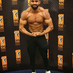 Posing in front of the National Athletic Committee (NAC) banner. This front relaxed pose is the first impression you give the judges, showcasing symmetry and proportion.