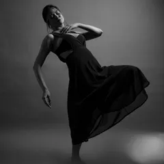 A black and white study in grace and movement. The model's pose, combined with the soft, foggy lighting, creates a dreamy and ethereal atmosphere, highlighting the elegant lines of her body and the dress.